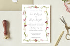 Printable pink and green floral wedding invitation with a delicate botanical border and elegant script names, styled beside an envelope, wax seal stamp and gold scissors for a romantic wedding stationery flat lay.