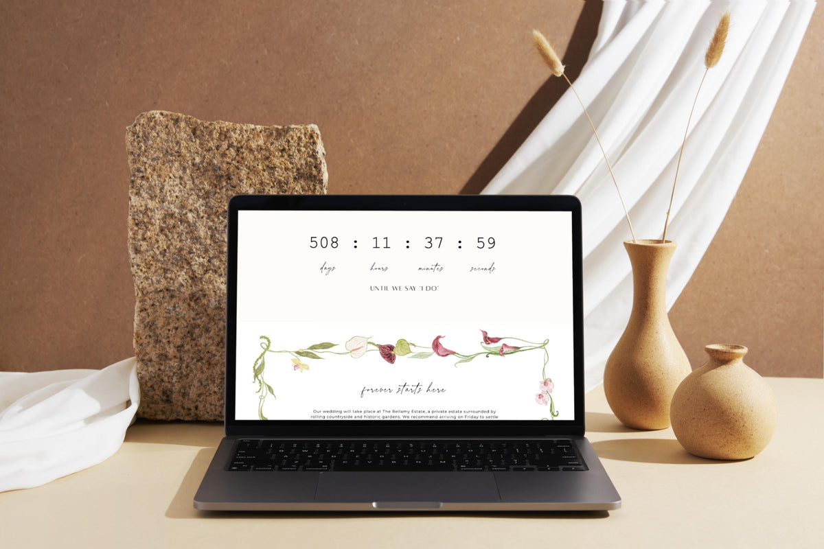 Wedding website template displayed on a laptop beside neutral ceramic décor, showing a wedding date and floral details in an elegant, minimal style.