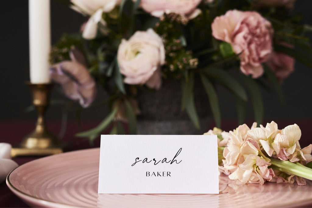 Modern flat wedding name card template with calligraphy guest name, styled on a blush plate with romantic pink wedding flowers.