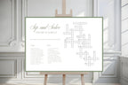 Sage bordered wedding crossword game sign displayed on an easel in a bright, elegant indoor wedding venue with white panelled walls.