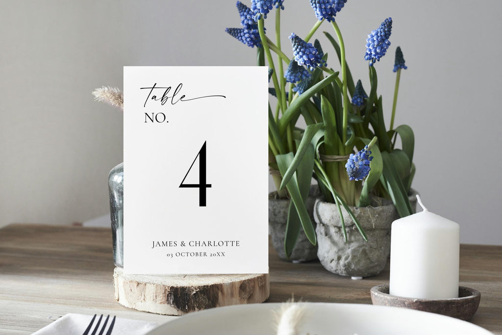 Modern wedding table number card template styled on rustic wooden centerpiece with flowers – editable black and white Canva design for elegant reception tables.