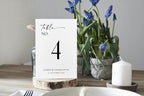 Modern wedding table number card template styled on rustic wooden centerpiece with flowers – editable black and white Canva design for elegant reception tables.