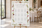 Botanical wedding seating chart template on a wooden easel at an elegant reception, featuring guest names grouped by table within a burgundy calla lily and green foliage border.