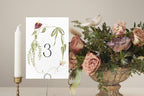 Floral wedding table number three with delicate green vines and burgundy flowers, styled beside a romantic garden-inspired centrepiece.