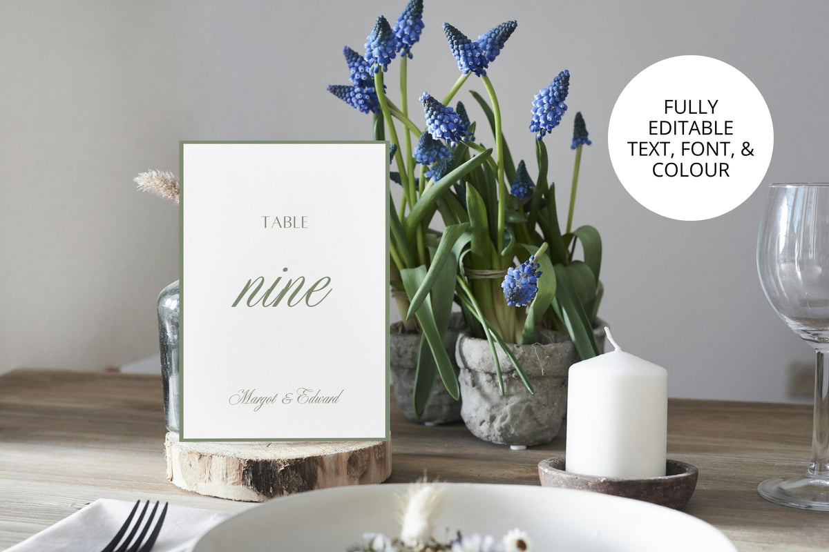Editable sage green wedding table number template displayed beside blue flowers and a white pillar candle, with a callout highlighting customisable text, fonts and colours for personalised wedding reception stationery.