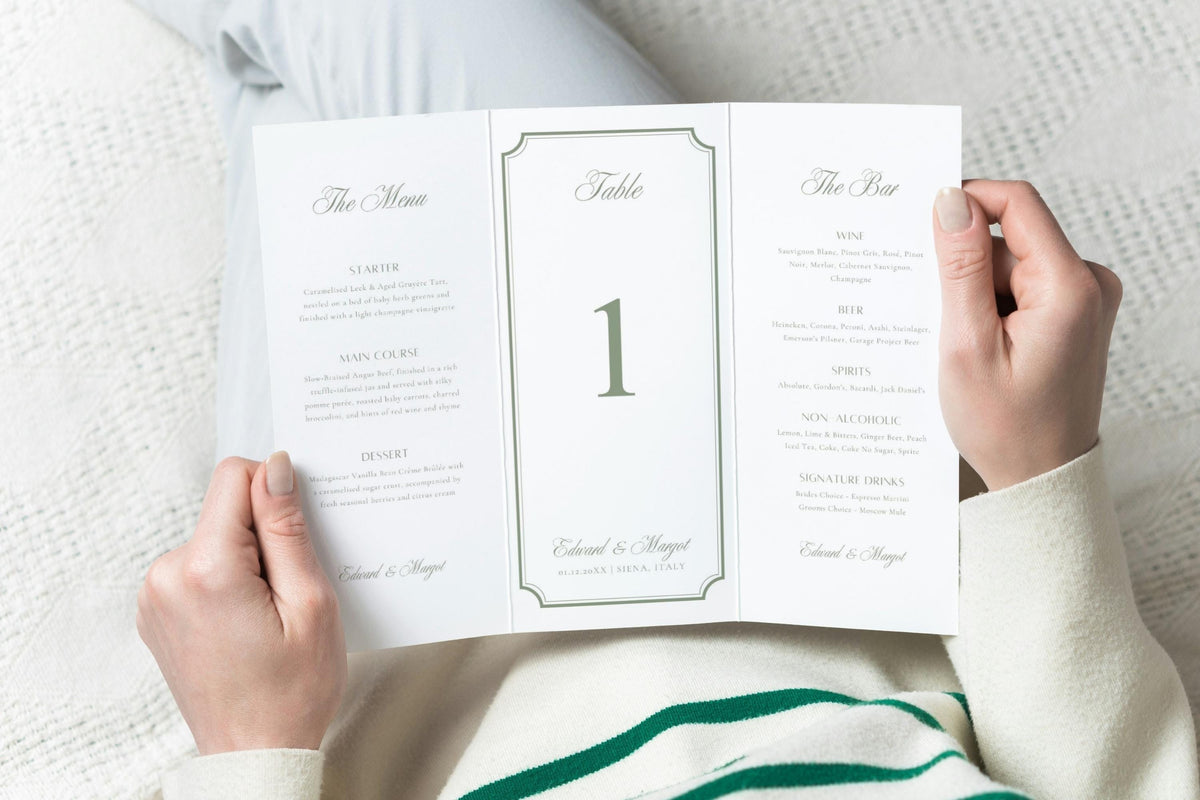 Unfolded three-panel wedding table stationery held in hands, featuring a wedding menu, central sage green table number and bar menu with romantic script typography and a classic decorative border.