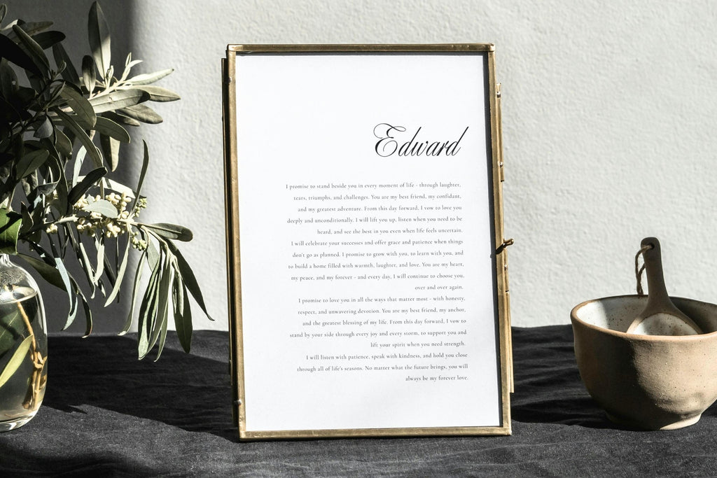 White wedding vows keepsake print with an elegant script name and black vow text in a slim gold frame, styled with greenery for romantic wedding vow display inspiration.