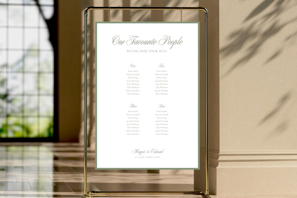 Sage green wedding seating chart displayed inside a gold frame at a sunlit venue entrance. Elegant old money wedding reception table plan with romantic script lettering and guest names arranged beneath table numbers.