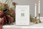 Printable sage green honeymoon fund wedding sign with a QR code, displayed beside burgundy flowers and white taper candles for an elegant wedding gift table or reception display.