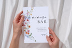 Hands holding printable mimosa bar sign with wildflowers, editable Canva bridal shower drinks station sign, modern boho wedding bar signage template