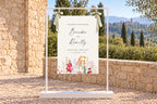 Printable wedding welcome sign on an easel at an outdoor stone venue, with colourful floral artwork, personalised script names and a scenic garden backdrop.