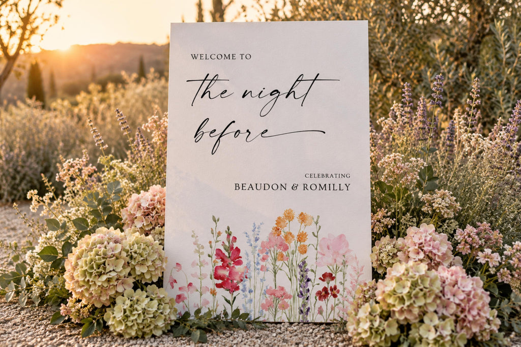 A1 rehearsal dinner welcome sign with colourful floral artwork, displayed on an easel in a garden wedding setting with pink and white flowers.