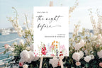 Floral rehearsal dinner welcome sign displayed outdoors beside white flowers, with a blue coastal wedding backdrop.