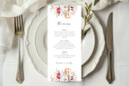 Floral wedding menu card displayed on a white plate at an elegant reception table, featuring a colourful pink and coral flower design with matching wedding stationery.