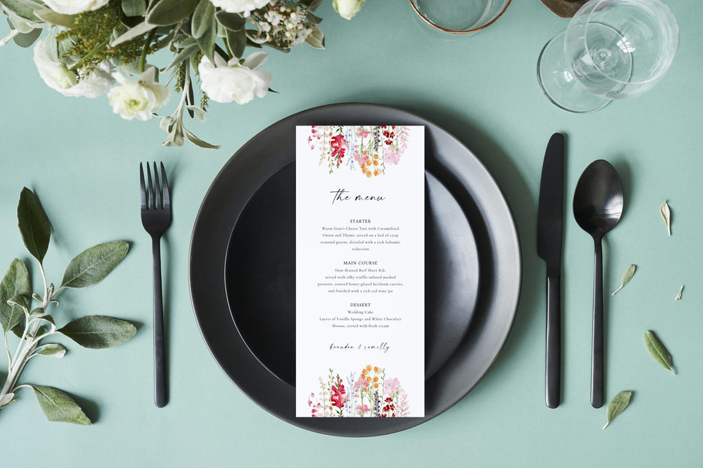 Pink and coral floral wedding menu card displayed on a black plate with dark cutlery and greenery, showing a modern wedding table stationery design.