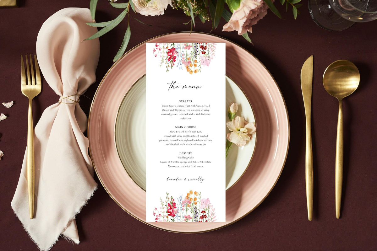 Long floral wedding menu card styled on a blush pink plate with gold cutlery and soft neutral linen for an elegant spring or garden wedding reception.