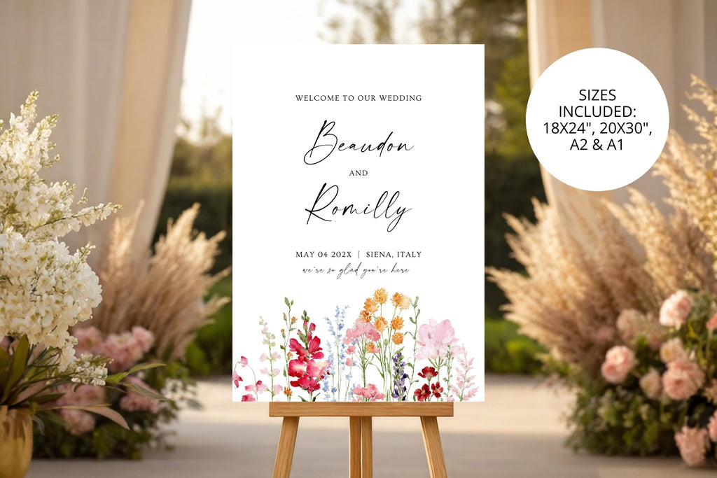 Floral wedding welcome sign displayed on an easel among warm-toned grasses and flowers, with a colourful garden design and personalised wedding names.