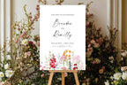 Editable wedding welcome sign styled in a lush garden setting, surrounded by flowers and greenery, with elegant script names and a romantic floral border.
