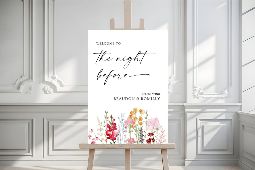 Close-up of a colourful floral rehearsal dinner welcome sign on an easel against a white panelled wall.