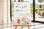 Editable rehearsal dinner welcome sign featuring colourful flowers, shown on an easel beside a bright outdoor wedding reception.