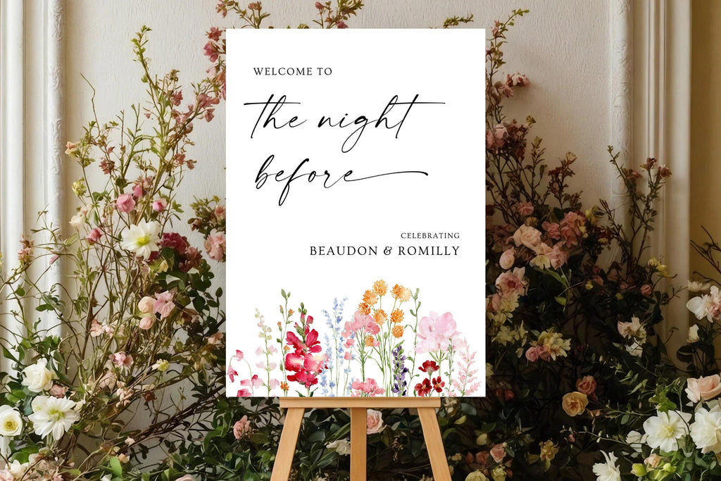 Rehearsal dinner welcome sign with a bright floral design, displayed among garden flowers and greenery for a romantic wedding celebration.