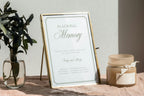 In loving memory wedding sign with sage green lettering and a fine border in a gold frame, displayed beside greenery and candles for a thoughtful wedding memorial table.
