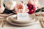Simple folded wedding place card template with editable calligraphy font, displayed on vintage inspired plate with neutral flowers