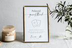 Framed editable Polaroid guestbook sign template with heart photo icon, displayed in a minimalist wedding setup with candles and greenery - perfect for a DIY photo guest book station.