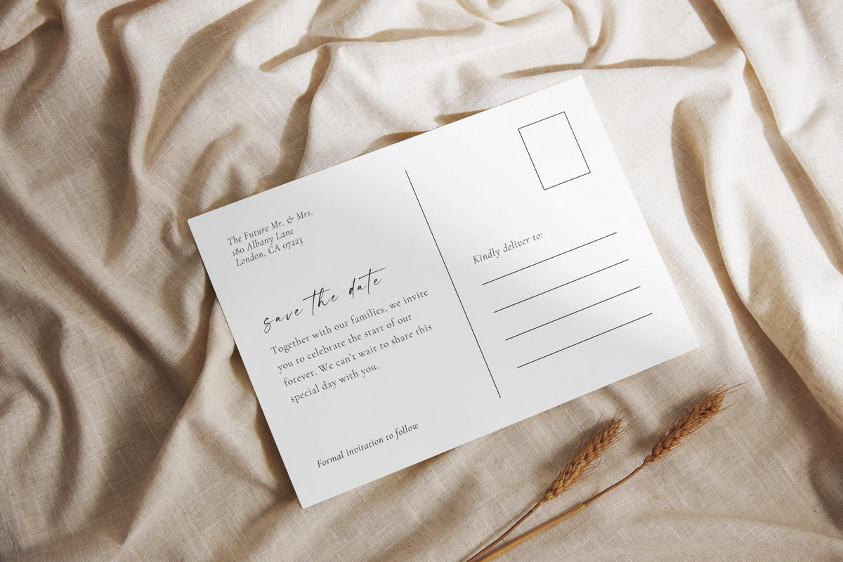 Flat lay of minimalist save the date postcard on beige fabric with handwritten script, perfect for timeless modern wedding invitation photo cards.