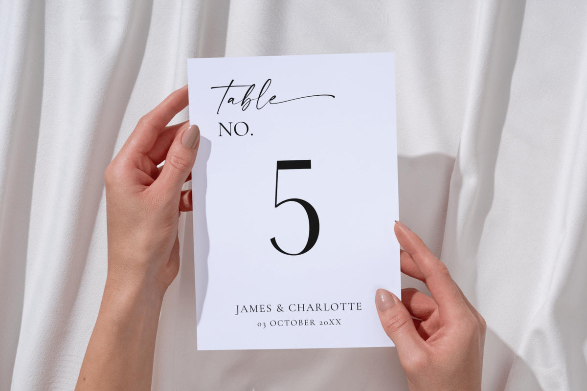 Hands holding minimalist wedding table number template – editable black and white Canva design, printable reception table signs for DIY wedding décor.