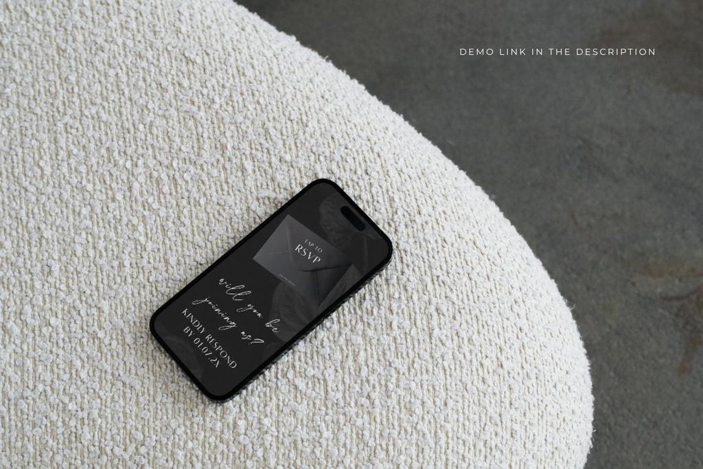 Mobile wedding website preview on a smartphone resting on textured white fabric, showing a dark wedding details page for guests to view online.