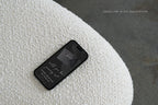 Mobile wedding website preview on a smartphone resting on textured white fabric, showing a dark wedding details page for guests to view online.