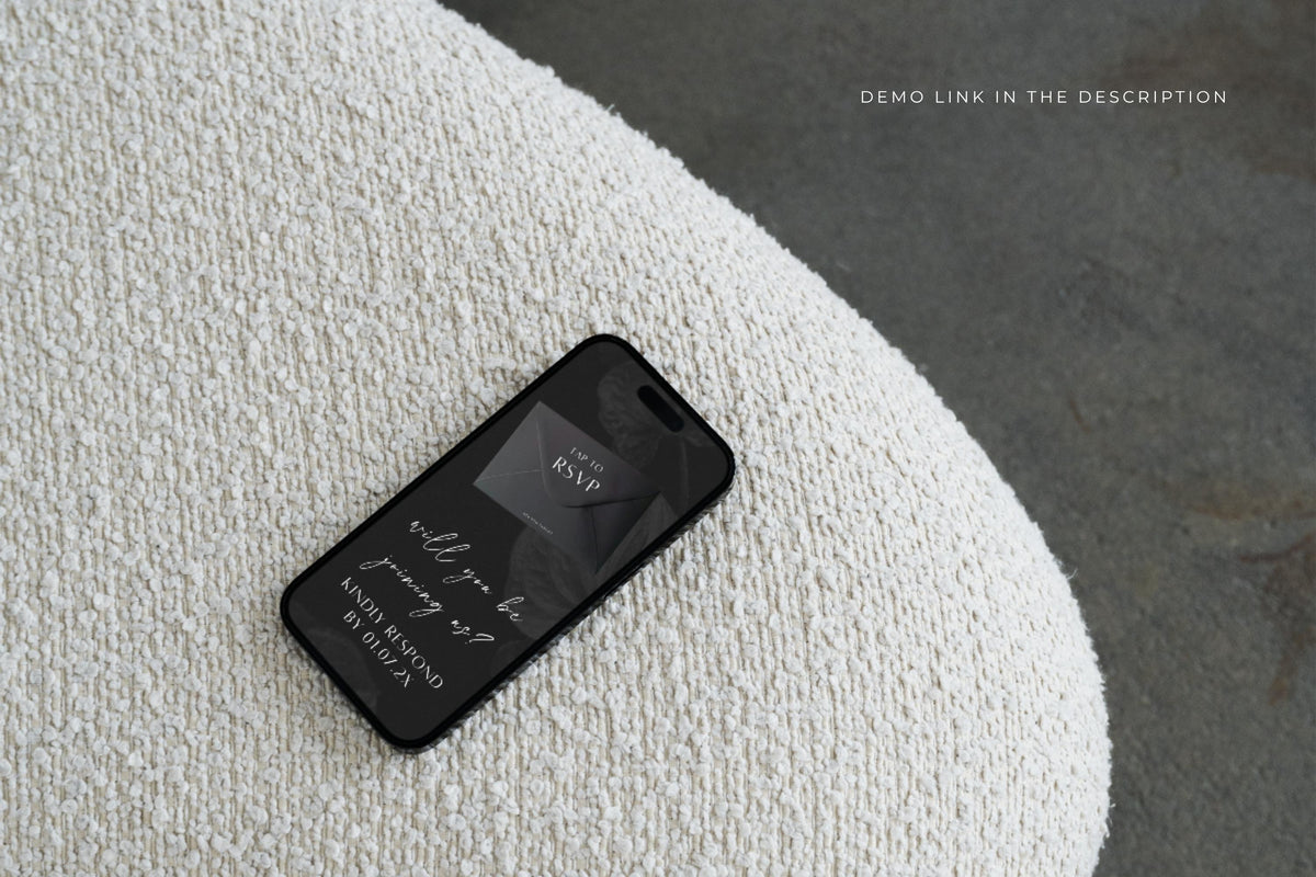 Mobile wedding website preview on a smartphone resting on textured white fabric, showing a dark wedding details page for guests to view online.