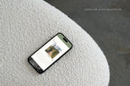 Mobile-friendly sage green wedding website template displayed on a phone resting on a textured cream surface, showing wedding location information and a venue photograph.
