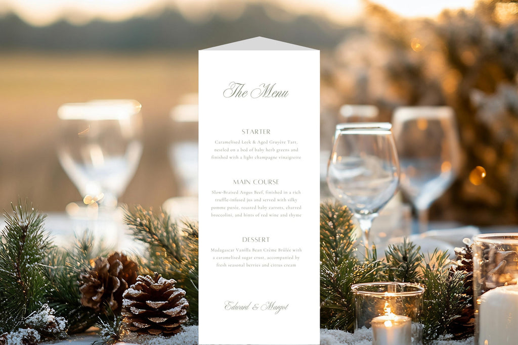 Classic trifold wedding menu displayed on an outdoor reception table with evergreen foliage, pine cones, candles and wine glasses, providing inspiration for elegant winter wedding table stationery.