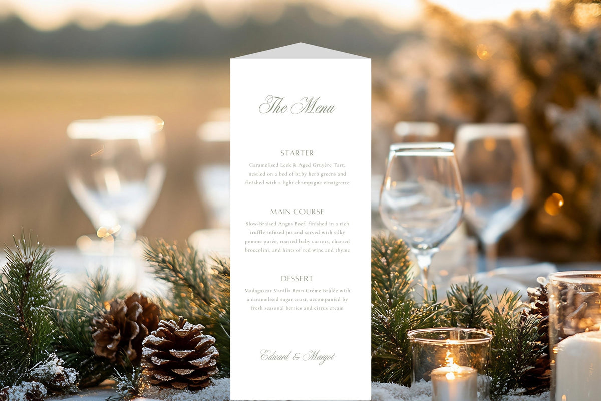 Classic trifold wedding menu displayed on an outdoor reception table with evergreen foliage, pine cones, candles and wine glasses, providing inspiration for elegant winter wedding table stationery.