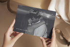 Black and white photo wedding thank you card held in hands, featuring a newlywed portrait, delicate script lettering and personalised names for a romantic editorial wedding thank you postcard.