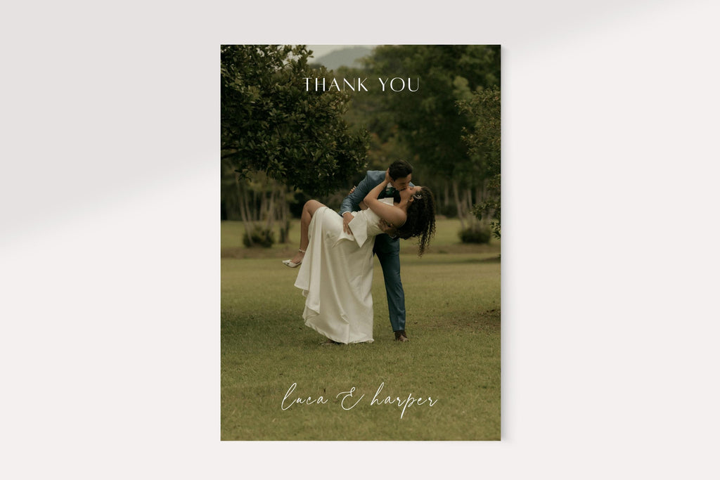 Full photo wedding thank you card front featuring a bride and groom embracing outdoors, with a delicate white thank you heading and handwritten style names. Minimal personalised newlywed photo card design.