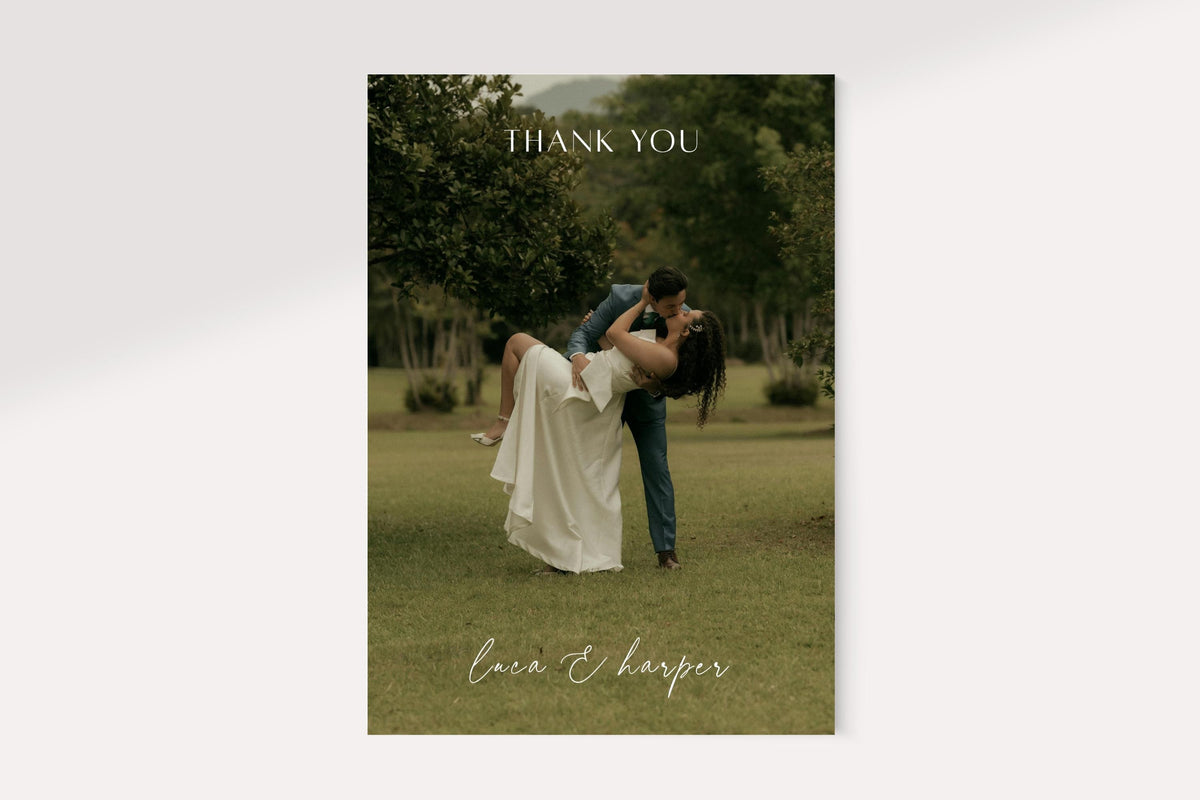 Full photo wedding thank you card front featuring a bride and groom embracing outdoors, with a delicate white thank you heading and handwritten style names. Minimal personalised newlywed photo card design.