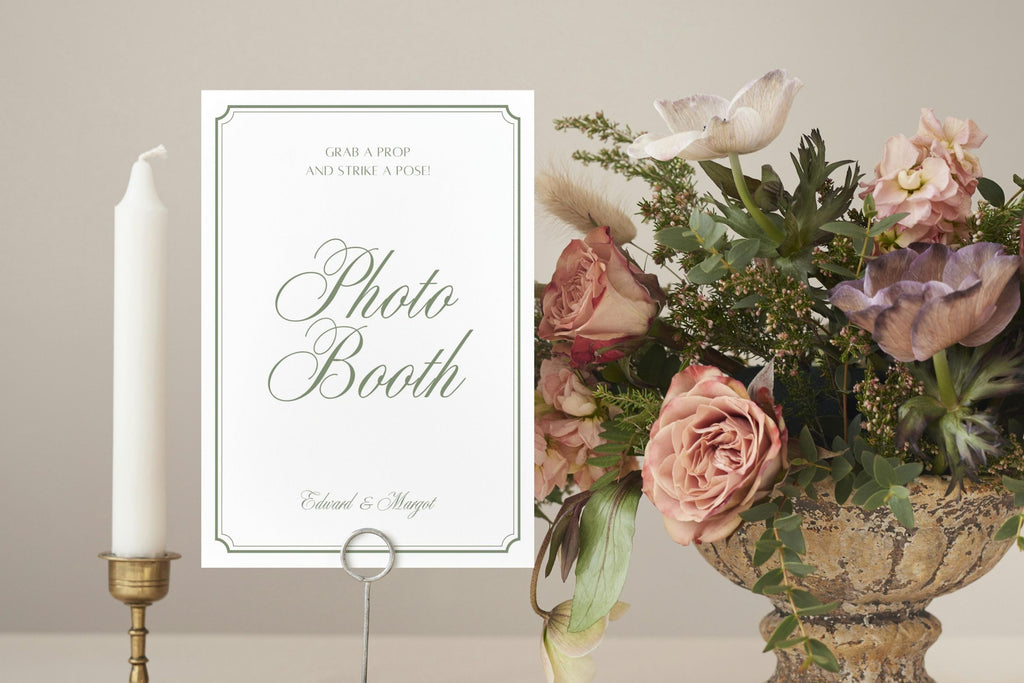Editable wedding photo booth sign in a simple white and sage green design, styled with candles and a colourful flower arrangement for a wedding reception.