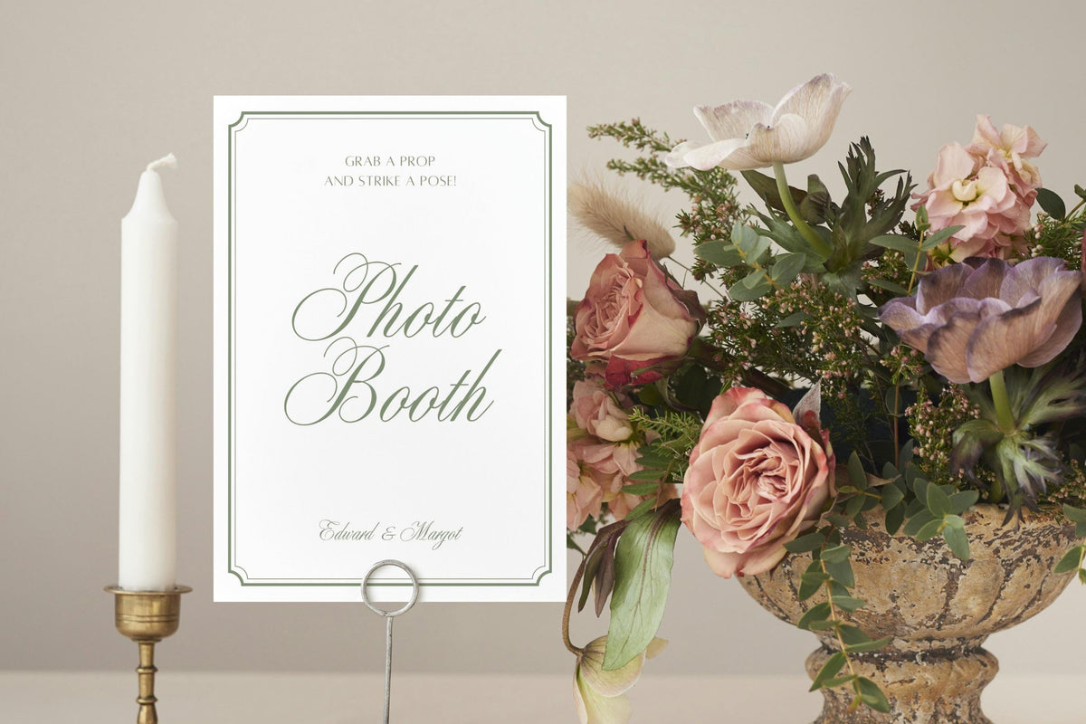 Editable wedding photo booth sign in a simple white and sage green design, styled with candles and a colourful flower arrangement for a wedding reception.