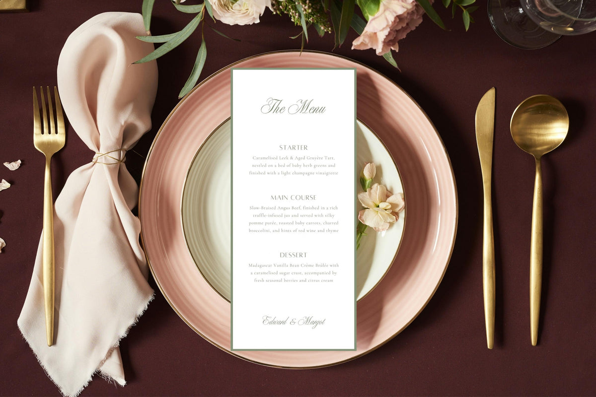 Sage green bordered wedding reception menu on layered blush pink plates with gold cutlery, a knotted ivory napkin and flowers against a burgundy tablecloth, styled for a romantic formal wedding dinner.