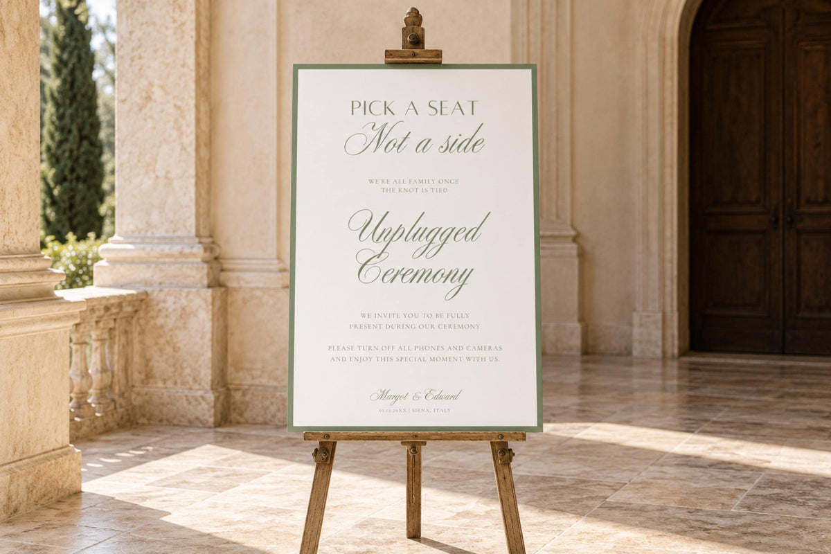 Sage green and ivory pick a seat not a side wedding sign combined with an unplugged ceremony message, displayed on a wooden easel outside a stone venue with elegant calligraphy and a classic border.