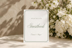 Please sign our guestbook wedding sign in sage green and ivory, displayed beside white flowers in a softly lit reception setting; editable wedding guestbook table sign.