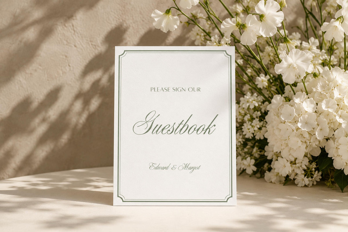 Please sign our guestbook wedding sign in sage green and ivory, displayed beside white flowers in a softly lit reception setting; editable wedding guestbook table sign.