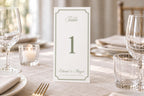 Sage green trifold wedding table number template with elegant script, a fine decorative border and ivory background, standing on a linen reception table with crystal glassware for an old money wedding.