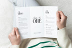 Hands holding an open trifold wedding menu and table number card, editable Canva wedding table decor, refined old money wedding menu and bar signage template