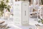 Elegant sage green wedding menu and table number trifold, showing the folded freestanding design styled with white flowers, candles and glassware on a classic wedding reception table.