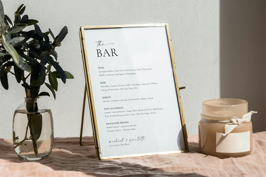Modern bar menu template for weddings displayed in gold frame with greenery, includes editable drink list, wine, and cocktail sections