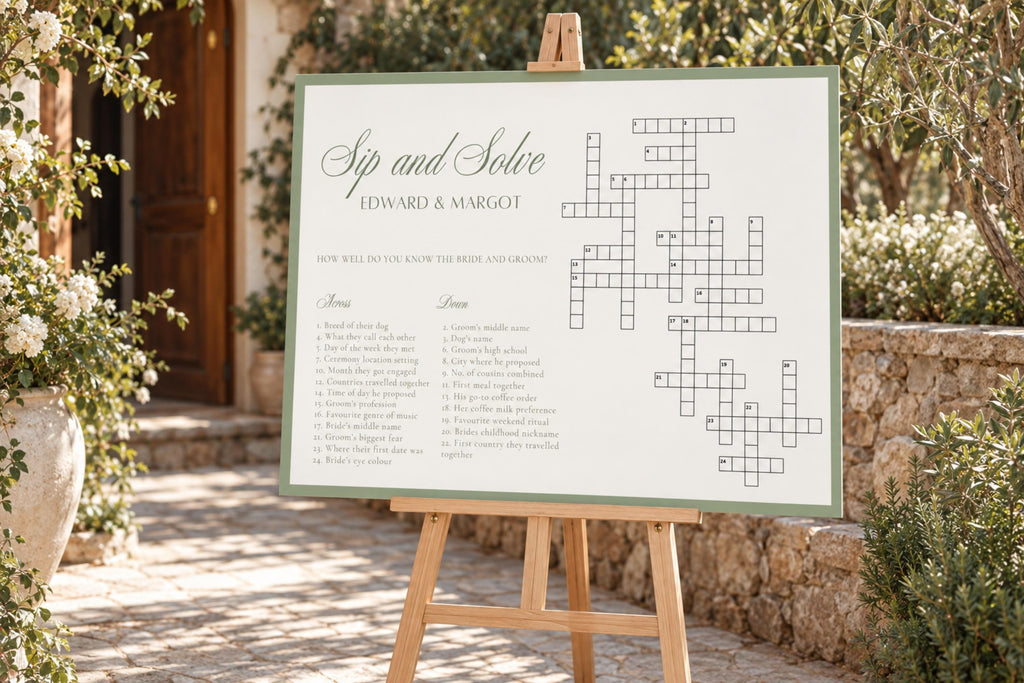 Editable sage green wedding crossword game sign on a wooden easel beside white flowers and greenery at an outdoor garden wedding.